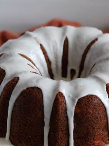 slice of gluten free apple bundt cake on white plate with red apple in background