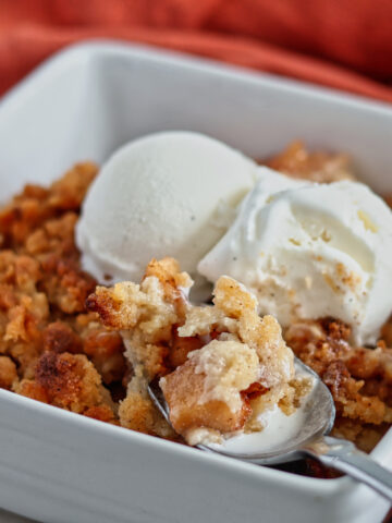 apple crumble in white square baking dish with two scoops of vanilla ice cream on top.