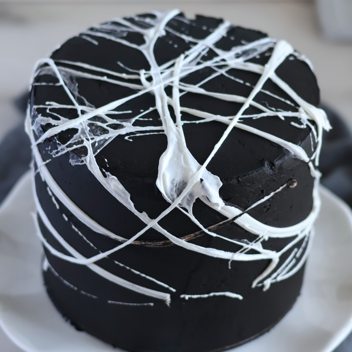 black layer cake on white cake stand with spiderwebs all over.