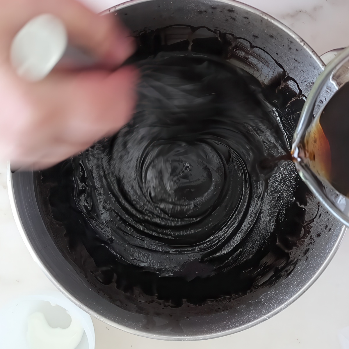 pouring brown liquid into black batter and whisking.