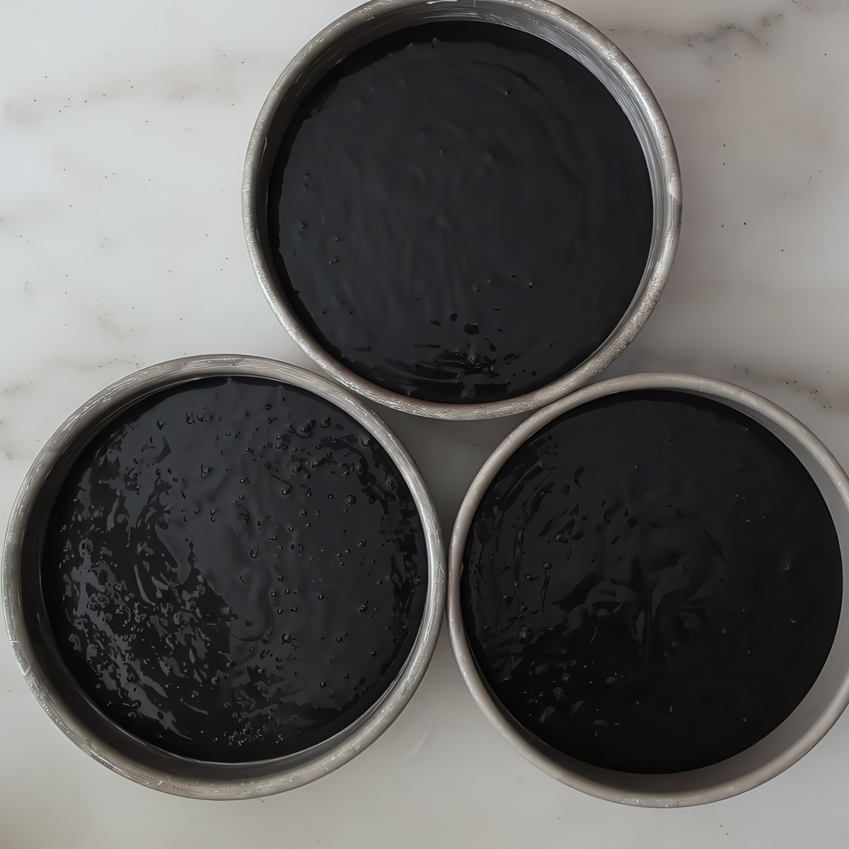 black batter in three round cake pans.