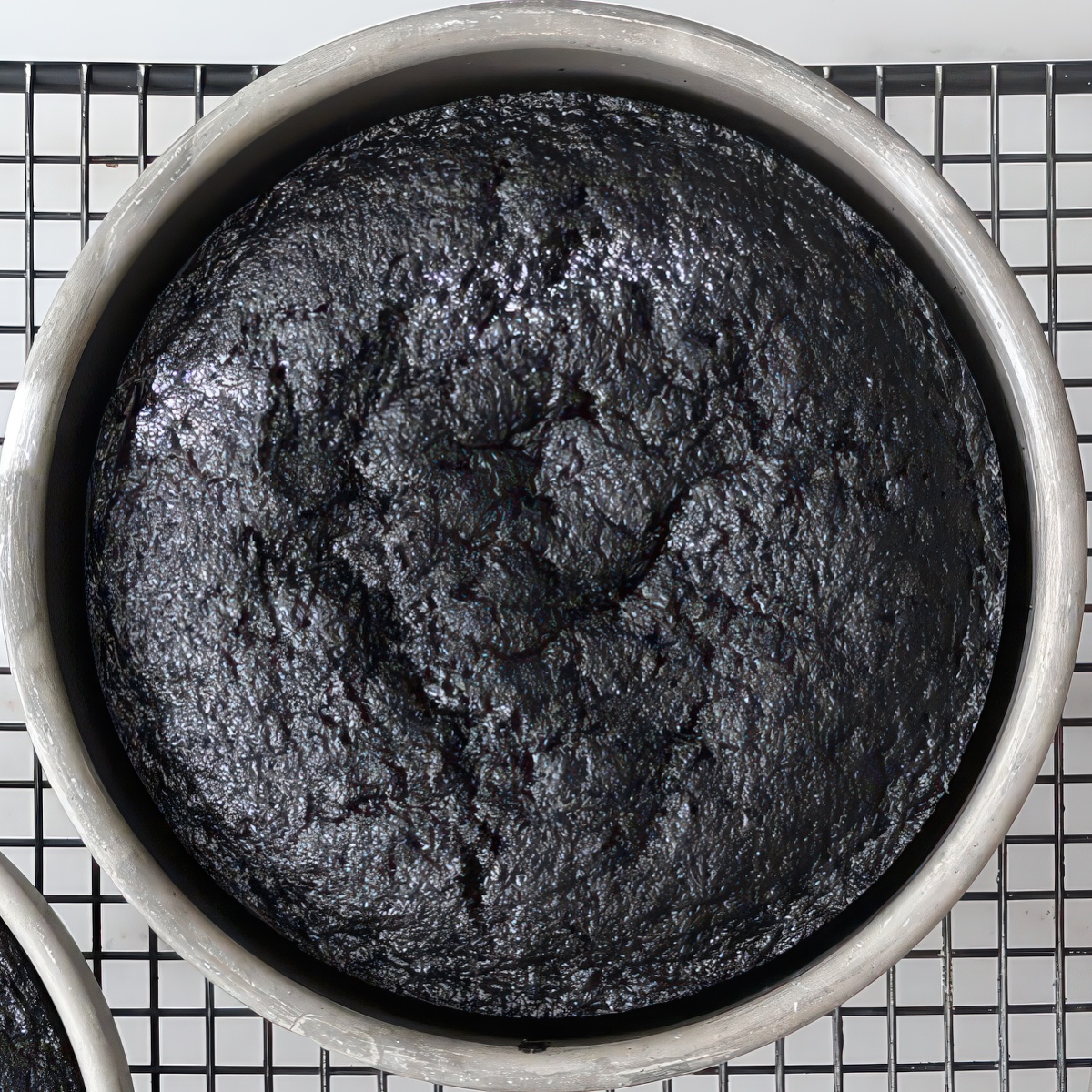 baked black cake in round pan on wire rack.