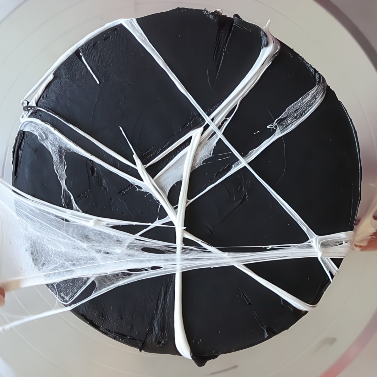 spreading marshmallow spider webs on top of black cake.