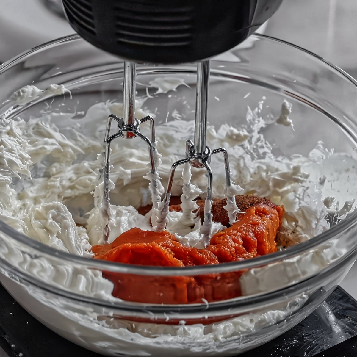 pumpkin puree on top of cream cheese in glass bowl with hand mixer.