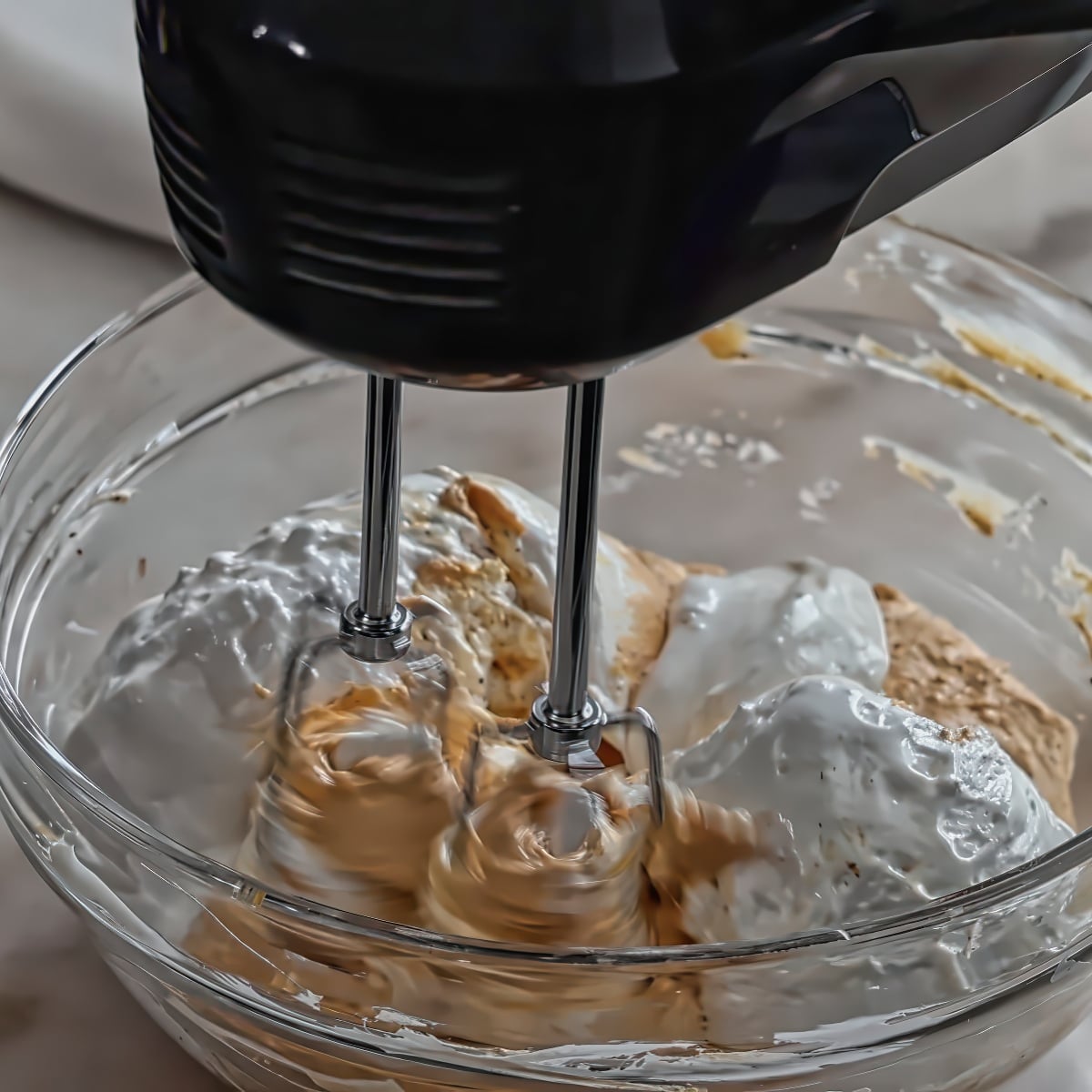marshmallow cream on top of orange dip in glass bowl with hand mixer.