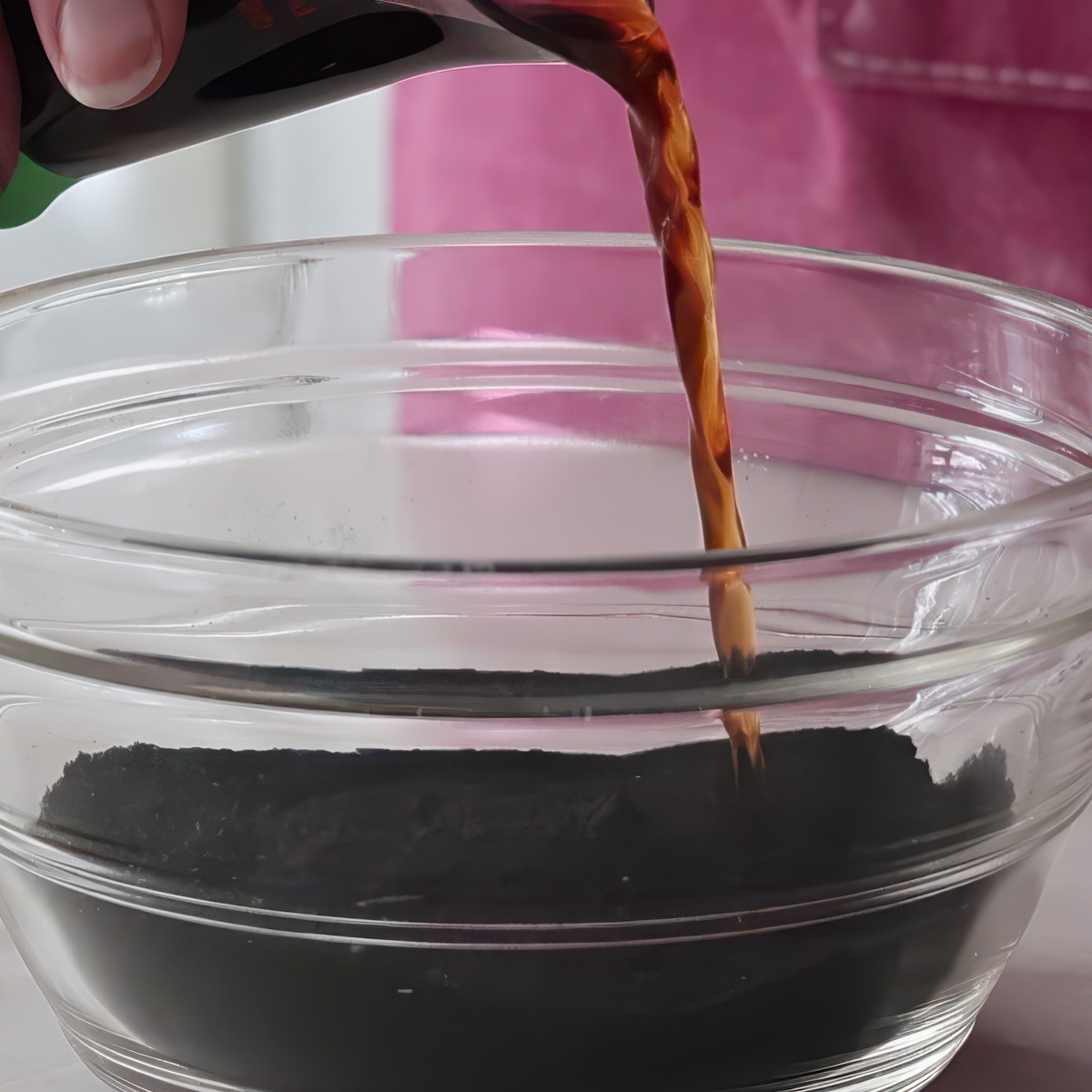 pouring coffee into black cocoa in glass bowl.