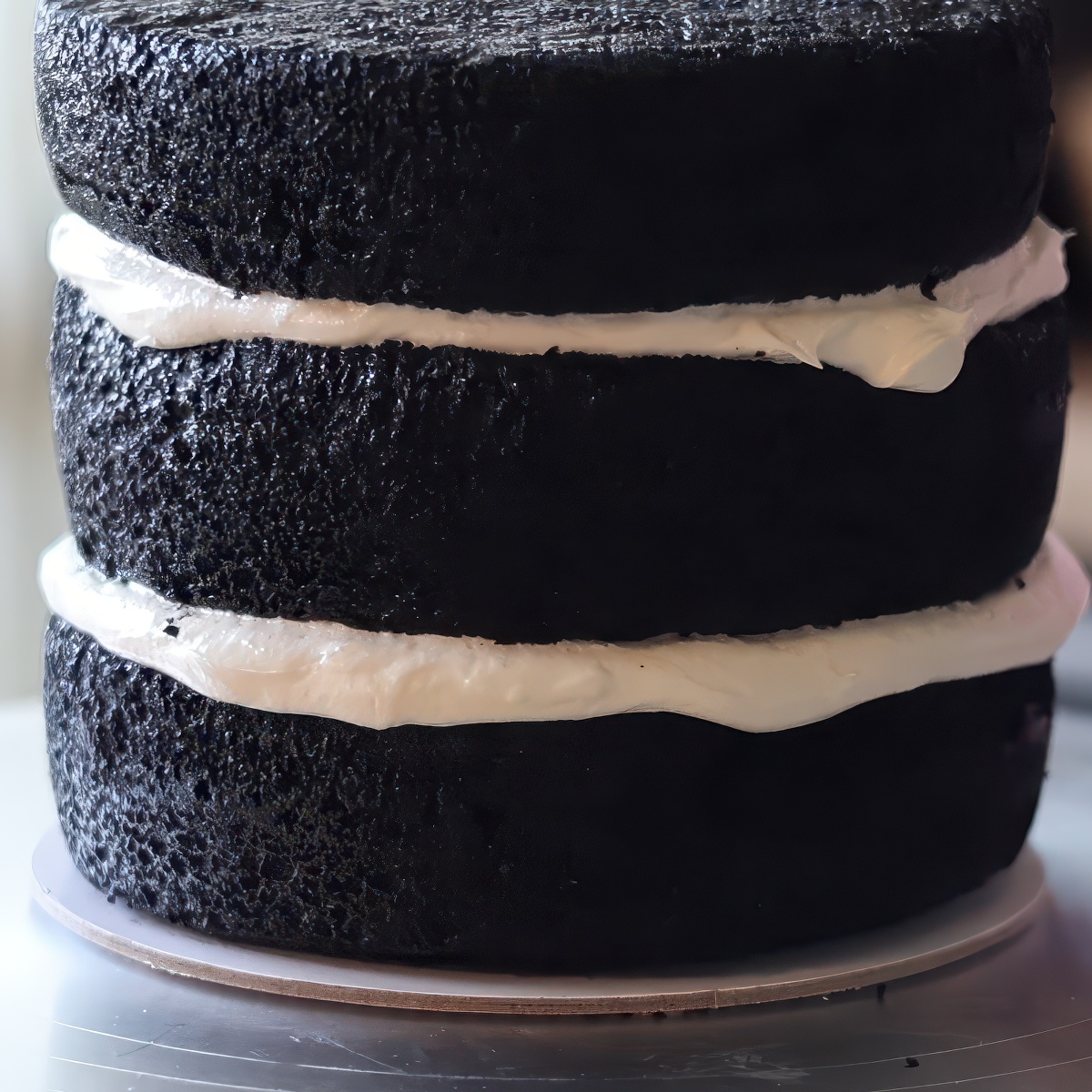 three black cakes stacked with white frosting in between.