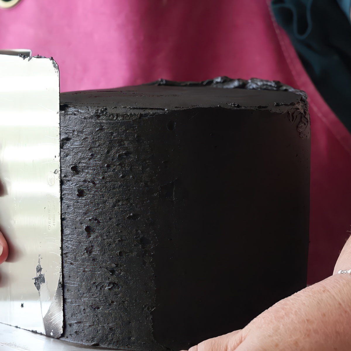 smoothing black frosting on cake with metal scraper.