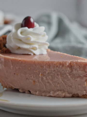 slice of pink pie on plate with whipped cream and one cranberry on top.