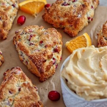 cranberry scones on light brown parchment with cranberries and orange slices.