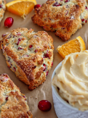 cranberry scones on light brown parchment with cranberries and orange slices.