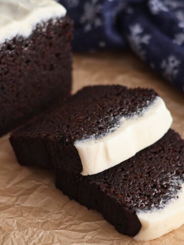 side view of sliced gingerbread loaf on brown paper with blue snowflake towel in the background.