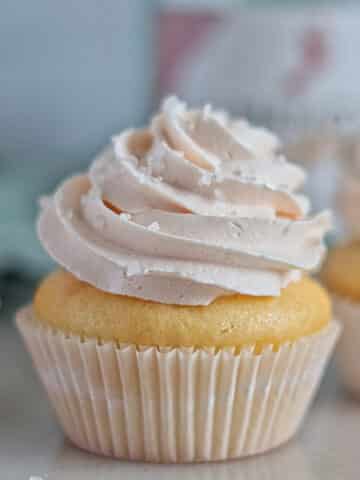 three champagne cupcakes in front of empty champagne bottle.