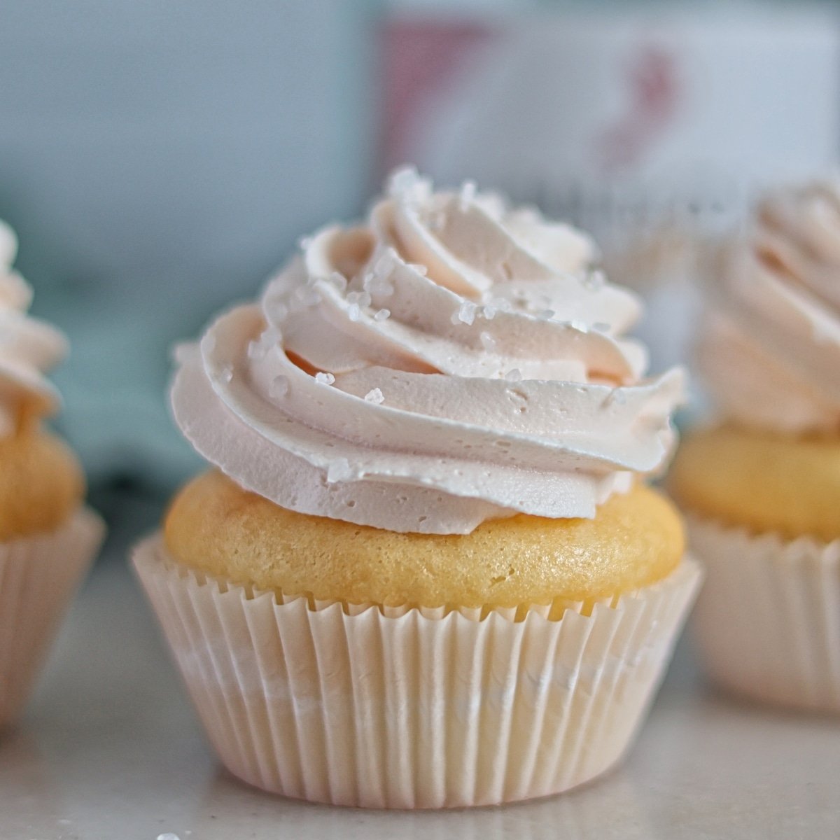 three champagne cupcakes in front of empty champagne bottle.