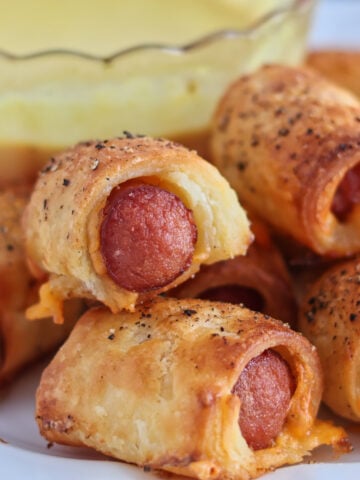 pigs in a blanket on white plate with mustard sauce.